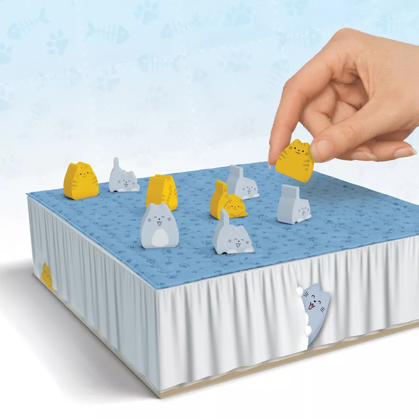 Hand placing a yellow cat figure on a blue and white surface with other cat figures.